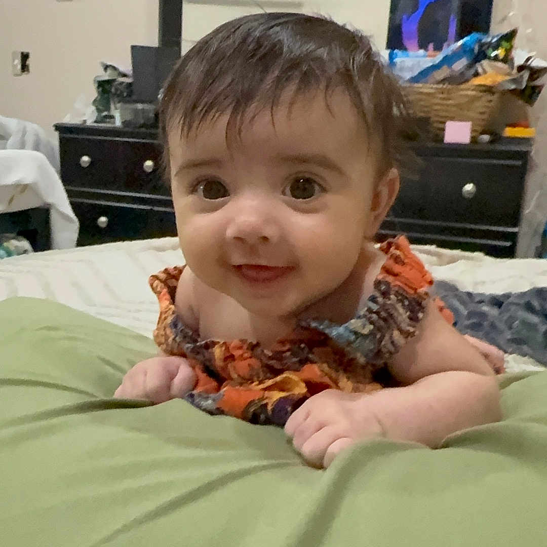 Willow is registered to the contest to win money with this photo: baby, infant, child, face, smile, eyes, hair, blanket, bed, dressing_table, mirror, room, furniture, home, curious, clothing, skin, hand, lying, indoors
