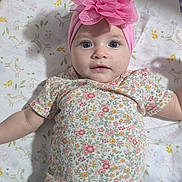 Amy is registered to the contest to win money with this photo: baby, infant, child, portrait, lying_down, headband, pink_flower, floral_clothing, green_pants, baby_bed, changing_mat, patterned_blanket, butterflies, flowers, indoor, close_up, wide_eyes, infant_fashion, adorable, photography