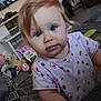 blonde_hair, blue_eyes, butterfly_pattern, carpet, child, close_up, couch, curious_expression, foot, furniture, indoor, ladybug_pattern, living_room, person, pink_shirt, playful, stuffed_animals, toddler, toys, young