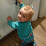 toddler, child, pajamas, cabinet, kitchen, wood_floor, curious, indoor, baby, footwear, toy_pattern, sweater, blond_hair, playful, crawling, young_child, home_interior, person, looking_back, floor
