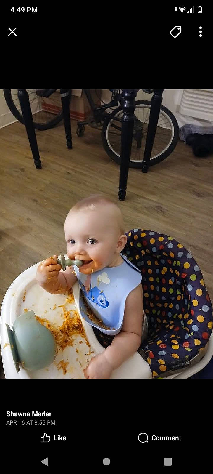 baby, bib, bicycle, chair, child, eating, face, floor, food, high_chair, indoor, messy, mouth, person, plate, polka_dot, spaghetti, spoon, toy, wooden_floor