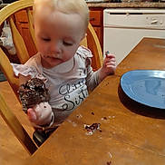Maylee joined the competition — help win amazing prizes! toddler, child, cupcake, chocolate, crumbs, kitchen, table, plate, chair, wooden_furniture, food, messy, eating, person, indoor, blond_hair, clothing, sitting, young_child, face