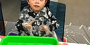 Elijah joined the competition — help win amazing prizes! black_sweater, boy, chair, child, door, expression, eyes, face, floor, floral_tablecloth, green_tray, hair, handwear, indoor, patterned_clothing, plastic_gloves, plastic_sheet, rosy_cheeks, table, trash_bin