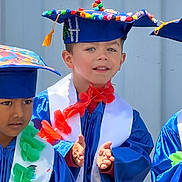 Elijah joined the competition — help win amazing prizes! child, children, graduation, cap, gown, celebration, clapping, smiling, colorful, blue, portrait, festive, outdoor, happy, young, sash, decorated_cap, event, person, toddler