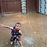 Elijah is registered to the contest to win money with this photo: child, water, playing, barefoot, smiling, life_vest, swim_shorts, wet_surface, concrete, fence, stone_pillar, outdoor, fun, summer, happy, boy, splash, water_stream, casual_clothing, daytime