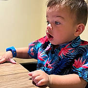 Elijah is registered to the contest to win money with this photo: boy, casual_wear, child, clothing, curious, expression, face, floral_pattern, hand, indoor, person, portrait, shirt, short_hair, sitting, skin, table, toddler, watch, wooden_surface