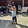 Elijah is registered to the contest to win money with this photo: bench, bubbles, casual_clothing, child, concrete, daytime, fence, fun, garden, grass, happy, joy, outdoor, person, play, shadow, sneakers, summer, sunlight, toddler