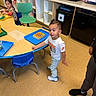 Elijah is registered to the contest to win money with this photo: child, children, classroom, table, chair, floor, toy, furniture, person, clothing, indoor, shoes, hair, face, expression, sitting, standing, playful, educational, learning