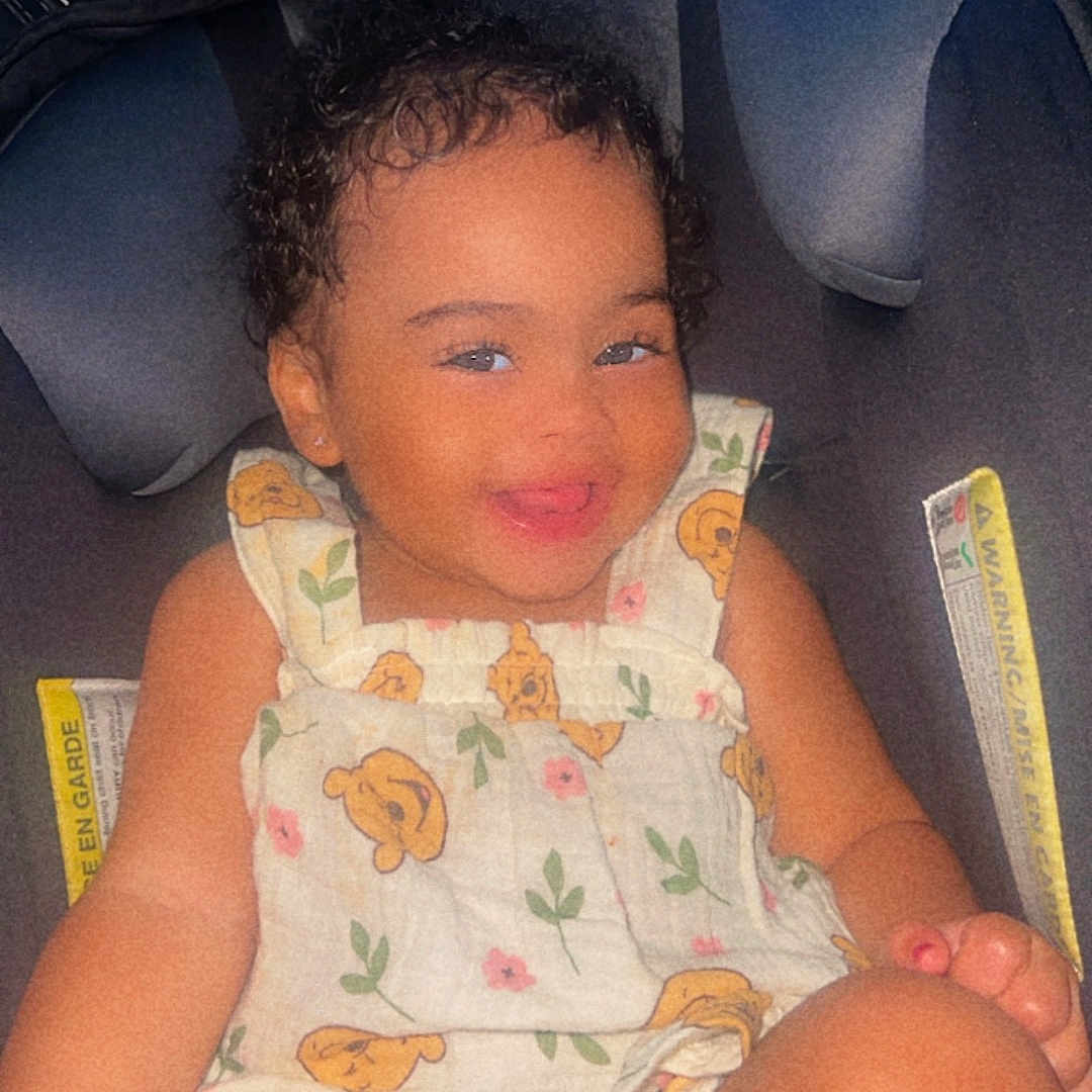 Jhlani Dockins joined the competition — help win amazing prizes! baby, bear_pattern, car_seat, child, clothing, curly_hair, cute, face, flower_pattern, happy, head, indoors, person, portrait, romper, seatbelt, sitting, skin, smile, toddler