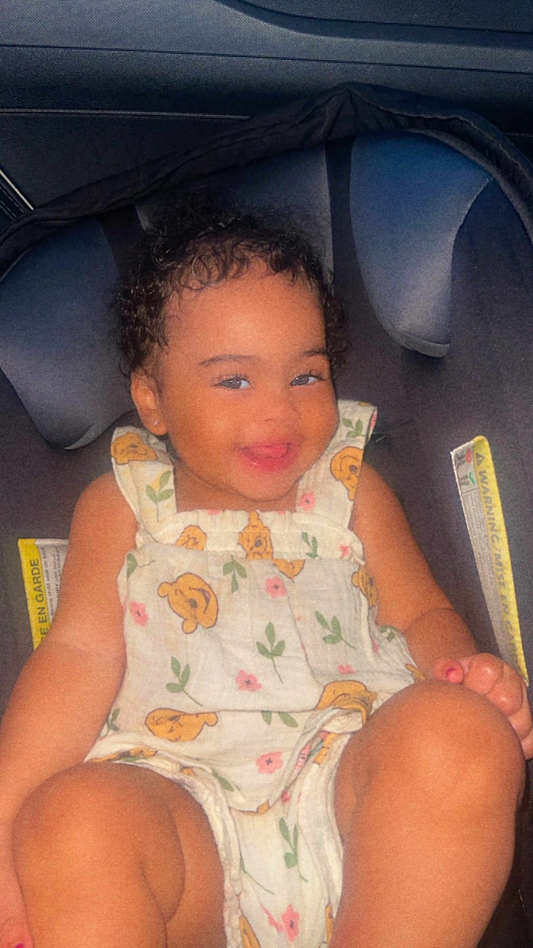 Jhlani Dockins joined the competition — help win amazing prizes! toddler, child, smile, car_seat, romper, flower_pattern, bear_pattern, curly_hair, happy, baby, seatbelt, clothing, sitting, indoors, person, cute, skin, face, head, portrait