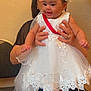 Jhlani Dockins joined the competition — help win amazing prizes! baby, child, dress, white_dress, flower_headband, smiling, happy, person, adult_hands, seated, indoor, chair, footwear, lace, celebration, cute, portrait, infant, holding, event