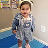 toddler, child, denim_jacket, bow, play_mat, classroom, poster, education, days_of_week, shapes, smiling, standing, shoes, socks, wall, outfit, happy, indoor, person, cute