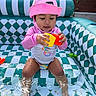 toddler, child, pink_hat, swimsuit, inflatable_pool, water, toys, yellow_toy, red_toy, sitting, playing, outdoor, summer, cute, water_play, pool_toys, colorful, baby, sun_hat, patterned_pool