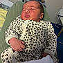 newborn, baby, sleeping, infant, leopard_print, onesie, clothing, hand, face, person, indoor, bed, blanket, plush_toys, nursery, soft_lighting, cute, peaceful, resting, child
