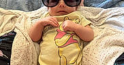 Brookelyn is registered to the contest to win money with this photo: baby, infant, sunglasses, yellow_onesie, blanket, blue_blanket, white_blanket, cute, child, person, indoors, laying_down, relaxed, soft_texture, clothing, smiling, portrait, small_hands, head, cozy