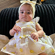 Brookelyn joined the competition — help win amazing prizes! baby, infant, child, portrait, sitting, indoor, living_room, black_cushion, floral_dress, headband, bow, toy_truck, yellow, baby_clothing, hands, legs, face, eyes, furniture, home