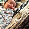 baby, newborn, smiling, wrapped, blanket, floral_pattern, cozy, woven_fabric, texture, sleeping, face, head, infant, person, comfort, soft, closeup, indoors, peaceful, resting