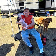 Brookelyn joined the competition — help win amazing prizes! baby, camper, camping, chair, dog, elderly_man, family, folding_chair, glasses, golden_retriever, grass, hat, jeans, nature, outdoor, person, pet, red_shirt, sneakers, sunlight