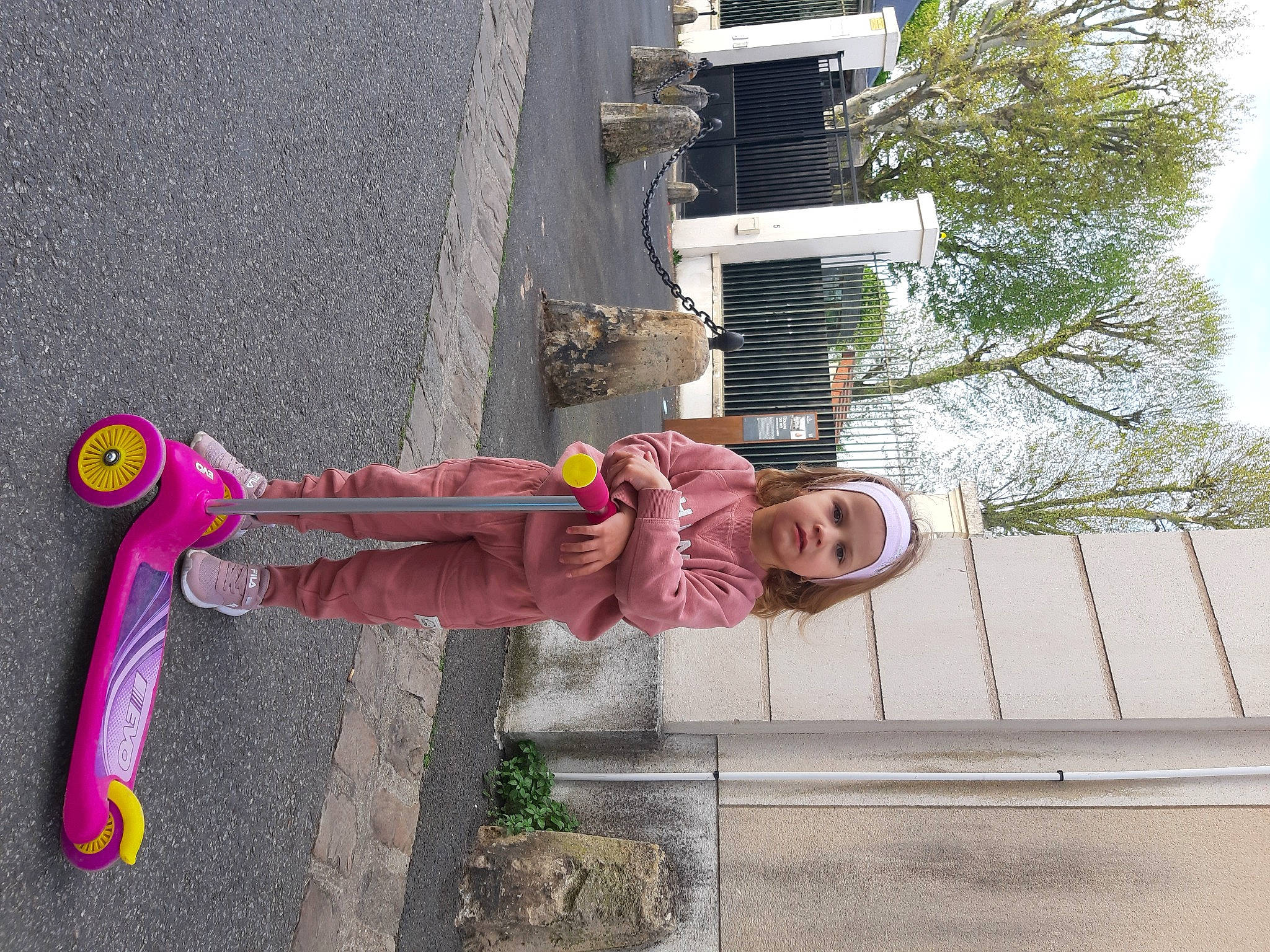 Gabriela participe au concours pour gagner de l'argent avec cette photo : asphalt, carmine, concrete, fun, headwear, house, magenta, pedestrian, person, plant, shadow, sidewalk, sky, smile, toddler, tree