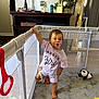 Lylah Ruth is registered to the contest to win money with this photo: baby, child, pacifier, playpen, plush_toy, carpet, lamp, plant, furniture, room, indoor, string_lights, clothing, person, toddler, standing, toy, decor, pacifier_in_mouth, smiling