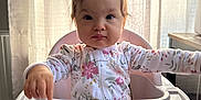 Lylah Ruth is registered to the contest to win money with this photo: baby, child, high_chair, snack, food, pajamas, floral_pattern, table, indoor, curtains, window, light, face, person, cute, expression, tabletop, feeding, infant, seat