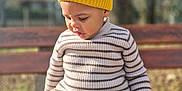 Dream a rejoint le concours — aidez-le/la à gagner de superbes lots ! toddler, child, yellow_hat, yellow_gloves, striped_sweater, beige_pants, wooden_bench, outdoor, autumn, sunlight, portrait, knitwear, cute, young_child, seated, focused_expression, daylight, nature_background, casual_clothing, seasonal