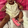 baby, child, infant, smiling, portrait, indoors, blanket, pink_blanket, headband, bow, dress, white_clothing, sitting, lying_down, bed, shoe, pink_shoe, happy, face, family_photo