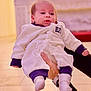 Aren joined the competition — help win amazing prizes! baby, infant, hand, clothing, white_outfit, purple_cuffs, socks, face, person, portrait, indoor, watch, floor, holding, cute, child, newborn, background, warm_lighting, expression