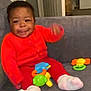 Leah-Eunice is registered to the contest to win money with this photo: baby, child, smiling, toy, couch, red_clothing, orange_clothing, socks, indoor, living_room, furniture, door, fridge, plastic_toy, happy, person, seated, motion_blur, home, cute