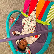 Leah-Eunice is registered to the contest to win money with this photo: baby, infant, play_mat, colorful, pajamas, toy, carpet, child, cute, indoor, floor, person, pattern, soft, fabric, lying_down, looking_up, small, cozy, playtime