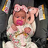 baby, infant, car_seat, pacifier, plush_toy, headband, onesie, floral_pattern, pink, cute, child, sitting, indoors, clothing, footwear, toy, comfort, adorable, portrait, young_child