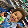 toddler, child, shopping_cart, grocery_store, smiling, curly_hair, toy, bottle, clothing, shelf, products, colorful, happy, person, retail, shopping, food, store, aisle, casual