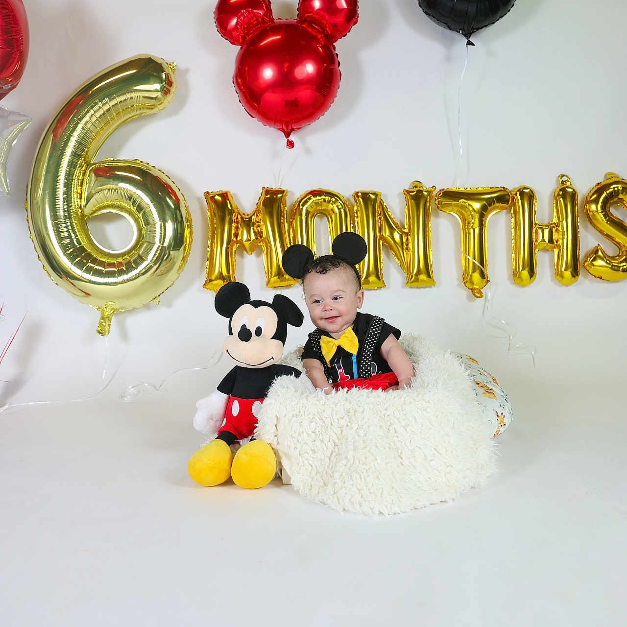 Kilynn is registered to the contest to win money with this photo: baby, balloons, birthday, black_clothing, blanket, celebration, child, costume, cute, decorations, festive, headband, indoor, mickey_mouse, party, plush_toy, red_shorts, smiling, white_background, yellow_bowtie