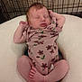 baby, closed_eyes, crib, cute, face, feet, floral_pattern, hands, indoors, infant, newborn, peaceful, pillow, pink_onesie, pose, relaxation, resting, skin, sleeping, wire_mesh
