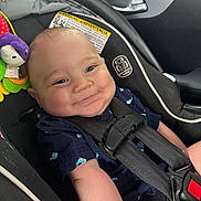 Faust is registered to the contest to win money with this photo: baby, car_seat, child, smile, straps, clothing, indoor, seatbelt, car_interior, happy, infant, person, cute, head, face, toy, purple, blue_shirt, safety, seat