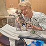 Blazey is registered to the contest to win money with this photo: woman, dog, hospital_gown, hospital_room, bed, water_bottle, cup, dessert, smile, short_hair, cabinet, sink, medical_equipment, hand, collar, small_dog, bed_rail, hat, blanket, indoor
