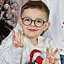 child, boy, glasses, sweater, spiderman, christmas, holiday, smiling, peace_sign, indoor, festive, winter, decorations, young_child, portrait, happy, seated, casual_clothing, cozy, family