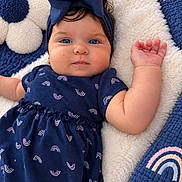 Valeria is registered to the contest to win money with this photo: adorable, baby, blanket, blue_eyes, bow, child, close_up, cozy, headband, indoor, infant, lying_down, navy_dress, plush, portrait, rainbow_pattern, safe, smiling, stuffed_animal, teddy_bear