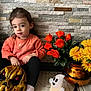 toddler, child, orange_sweater, black_pants, white_sock, halloween_mask, ghost_decoration, orange_flowers, yellow_flowers, flower_vase, copper_vase, stone_wall, indoor, sitting, toy, decoration, holiday, face, person, floor