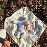baby, blanket, autumn_leaves, teddy_bear, knit_hat, knit_outfit, baby_clothing, person, hand, watch, outdoor, fall, nature, child, cute, soft_toy, lying_down, warm_clothing, family, tender_moment