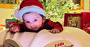 Waris is registered to the contest to win money with this photo: baby, santa_hat, christmas_tree, christmas_lights, holiday, book, reading, blanket, indoors, festive, gift_bags, decorations, child, holiday_spirit, cozy, winter, smiling, red_clothing, celebration, family