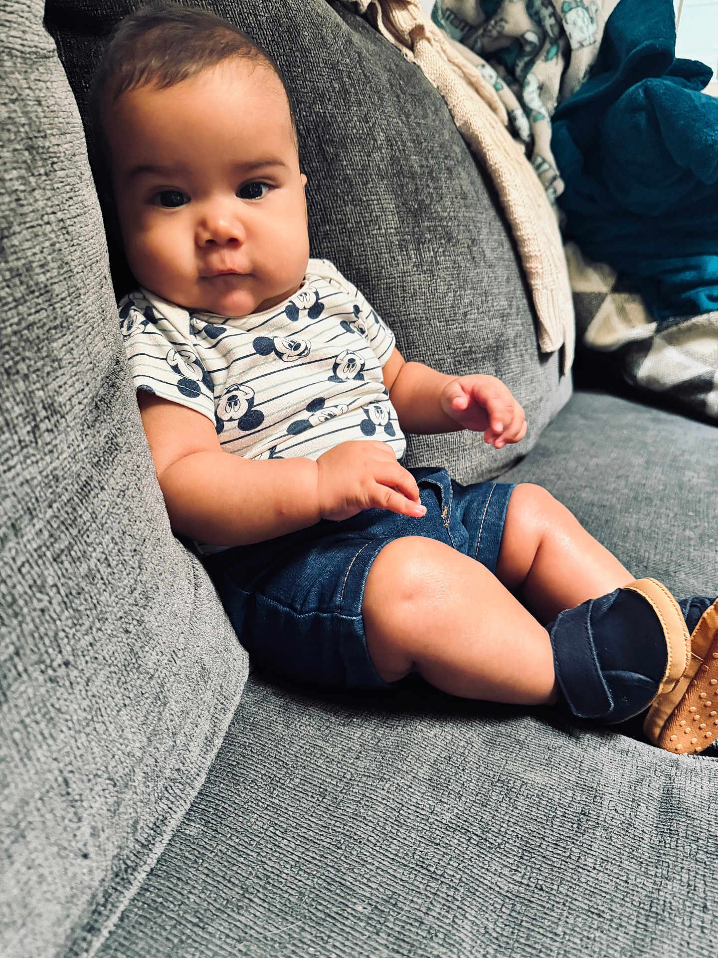 Gavin is registered to the contest to win money with this photo: baby, child, infant, couch, sofa, clothing, shorts, shirt, mickey_mouse, footwear, baby_shoes, indoor, portrait, sitting, curious, face, skin, cute, comfortable, home