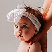 Eva a rejoint le concours — aidez-le/la à gagner de superbes lots ! baby, infant, headband, bow, big_eyes, portrait, studio_lighting, cute, chubby_cheeks, hand, supporting_hand, skin, face, hair, looking_away, expression, soft_background, child, newborn, close_up