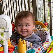 Adam is registered to the contest to win money with this photo: baby, child, smiling, face, toy, activity_center, indoor, clothing, seat, colorful, happy, expression, person, hair, furniture, play, cute, infant, pattern, background