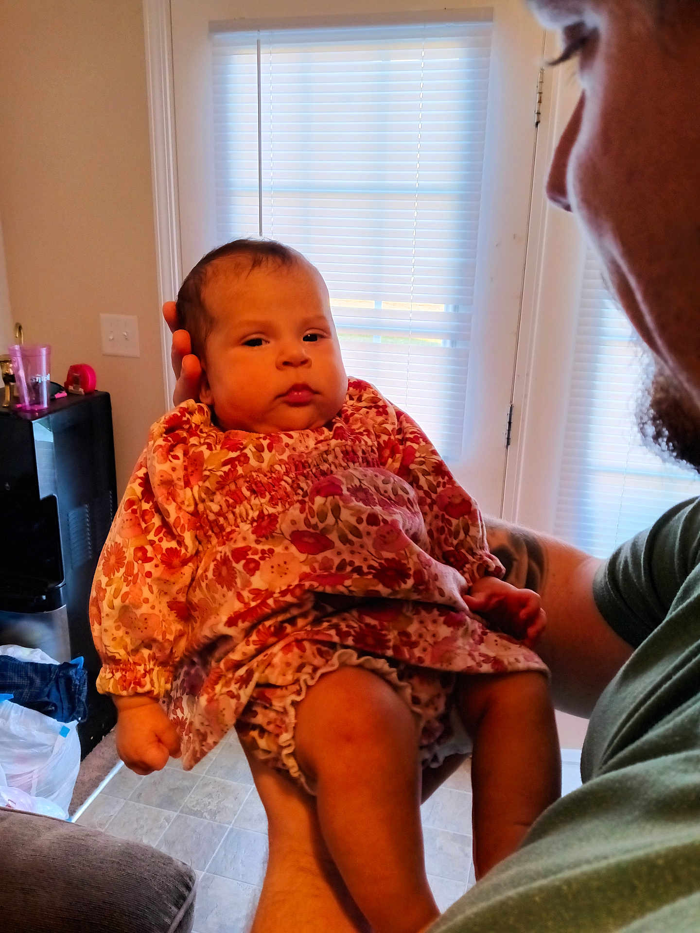 Julia joined the competition — help win amazing prizes! baby, infant, adult, holding, floral_dress, indoor, window, blinds, natural_light, person, face, arm, tattoo, floor, home, curtains, carpet, furniture, skin, clothing