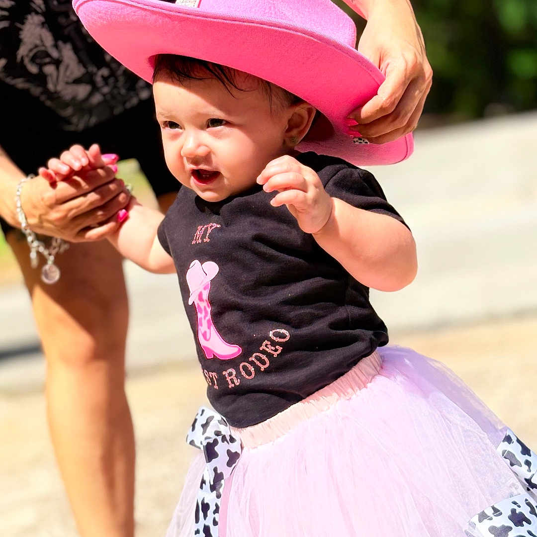 Aviah joined the competition — help win amazing prizes! adult_hand, background_blur, black_tshirt, child, cowboy_hat, cute, daylight, fashion, helping_hand, outdoor, person, pink_hat, playful, smiling, sunny, toddler, tutu_skirt, walking, warmth, young_child