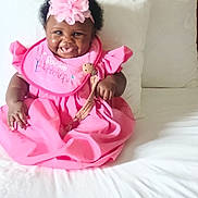 Allure joined the competition — help win amazing prizes! baby, child, infant, smiling, happy, portrait, pink_dress, flower_headband, teddy_bear, bed, pillows, bedding, indoors, sitting, dark_skin, curly_hair, facial_expression, baby_dress, celebration, cute