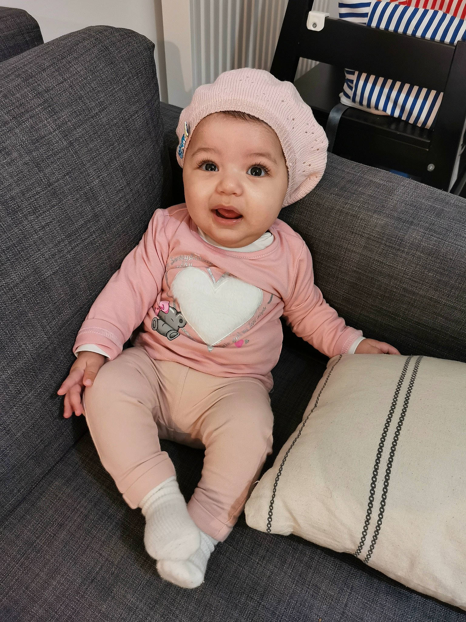 Djenna a rejoint le concours — aidez-le/la à gagner de superbes lots ! baby, baby_toddler_clothing, cap, comfort, couch, face, flooring, foot, headwear, human_leg, knee, linens, living_room, person, pillow, sitting, sleeve, smile, t_shirt, thigh