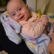 Emmilynn is registered to the contest to win money with this photo: baby, blanket, smiling, infant, person, indoor, soft_texture, happy, child, wrapped, cozy, human, portrait, wearing_clothes, arms, comfort, warm_light, closeup, cute, head