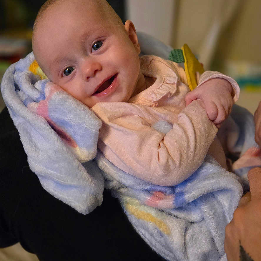 Emmilynn is registered to the contest to win money with this photo: baby, blanket, smiling, infant, person, indoor, soft_texture, happy, child, wrapped, cozy, human, portrait, wearing_clothes, arms, comfort, warm_light, closeup, cute, head